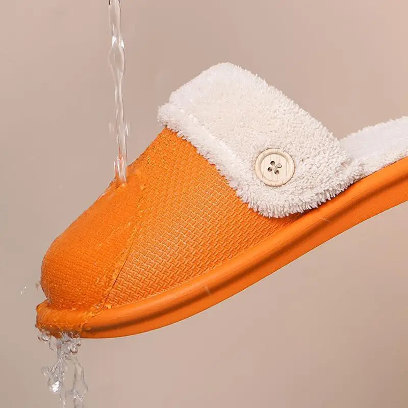 Orange winter slipper with a white fluffy towel-like lining and a decorative button made of washable plush material for women.