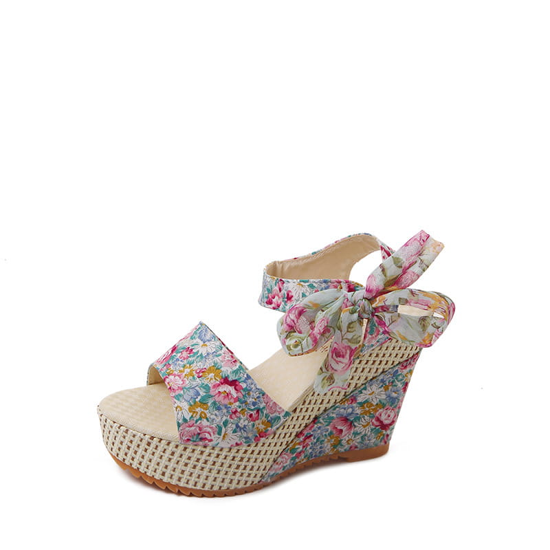 Floral bohemian platform wedge sandal with a floral pattern, woven mesh sole, and ankle strap tied in a bow.