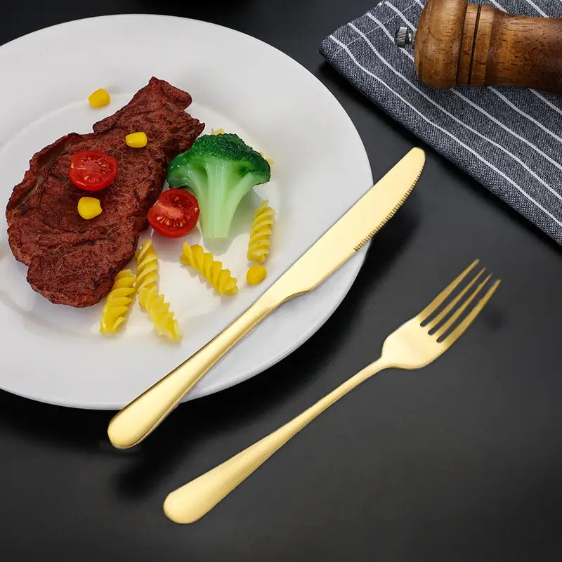 Rose gold stainless steel cutlery set with gold-finished dinnerware featuring a sleek knife and fork in a modern minimalist design.