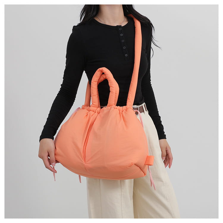 A lightweight quilted puffer tote bag made of nylon in soft peach color with a drawstring closure and matching handles.