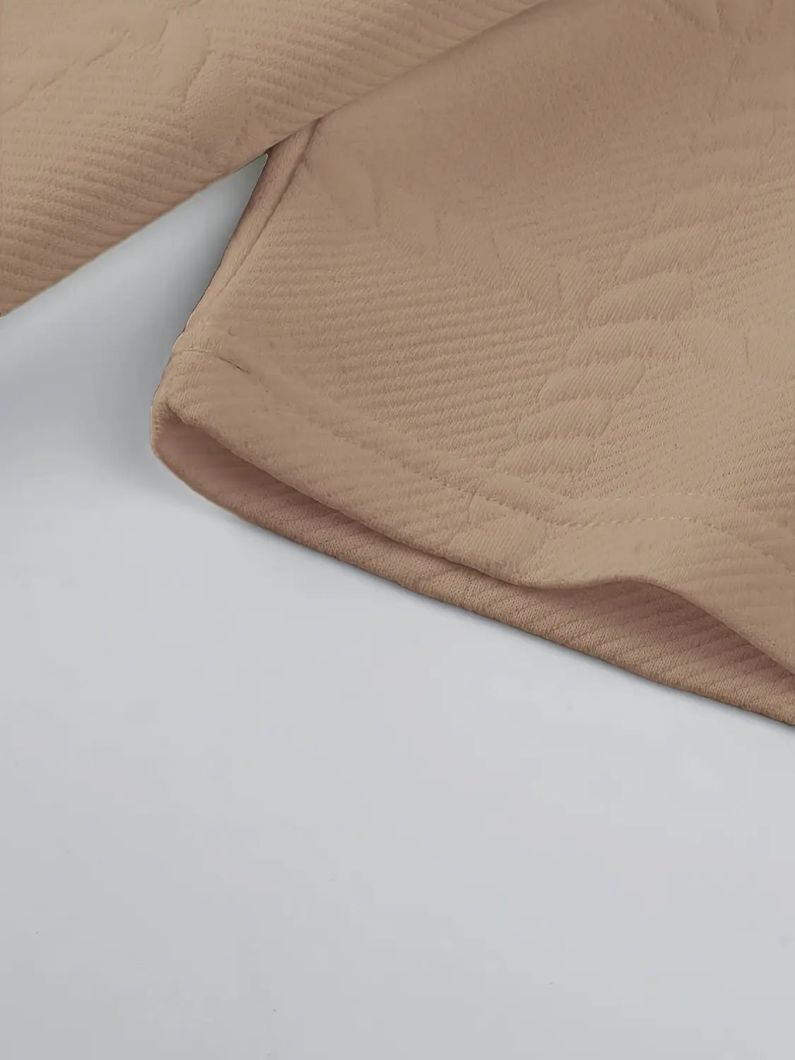Tela acolchada color beige con una sutil textura acanalada en una camisa tipo polo de manga larga con textura.