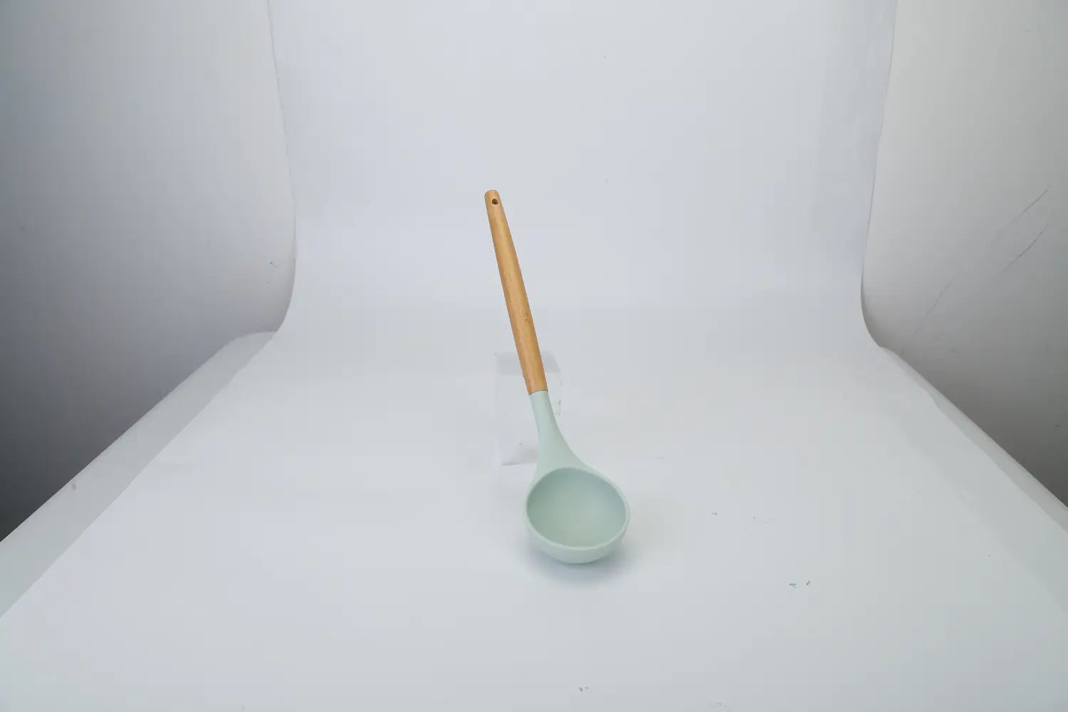 A light green silicone ladle with a wooden handle from a silicone cooking utensil set 11pc with wood handles.