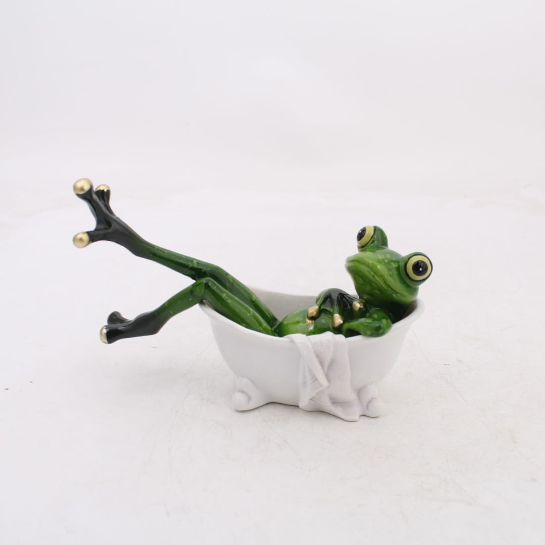 Grüne Resin-Froschfigur mit ausdrucksstarken Augen und goldbedüfteten Zehen, die auf einer kleinen weißen Badewanne für skurrile Wohnaccessoires-Statuen entspannt.