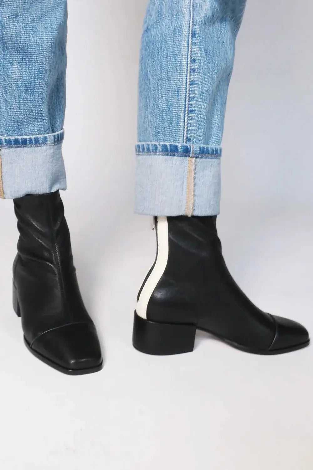 schwarze Stiefeletten aus Leder mit eckiger Zehenpartie, niedrigem Blockabsatz und kontrastierendem weißem Reißverschluss-Schieber, von der Rückseite dargestellt