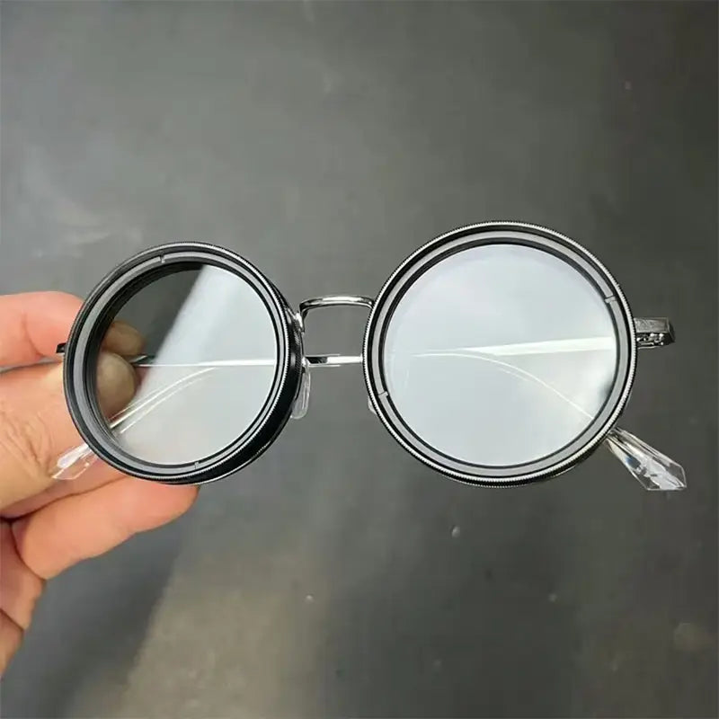 Lunettes de soleil rondes unisexes résistantes aux UV, avec lentilles transparentes à monture noire et branches métalliques terminées par un cristal.