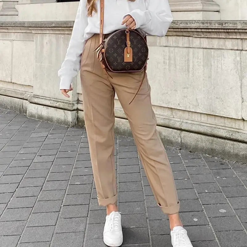Pantalon taille haute à plis plats et jambes droites assorti à un sac circulaire marron présentant un motif de monogramme et des anses en cuir beige.