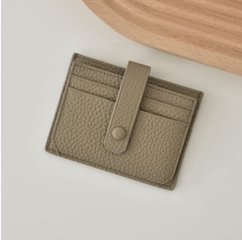 Beige ultra thin minimalist textured leather card holder with flap closure secured by a single button and strap.