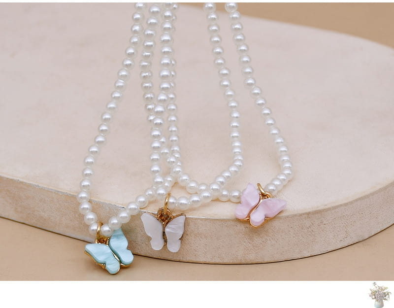 Three elegant pearl choker necklaces each featuring a delicate butterfly charm in pastel blue white and pink enamel.