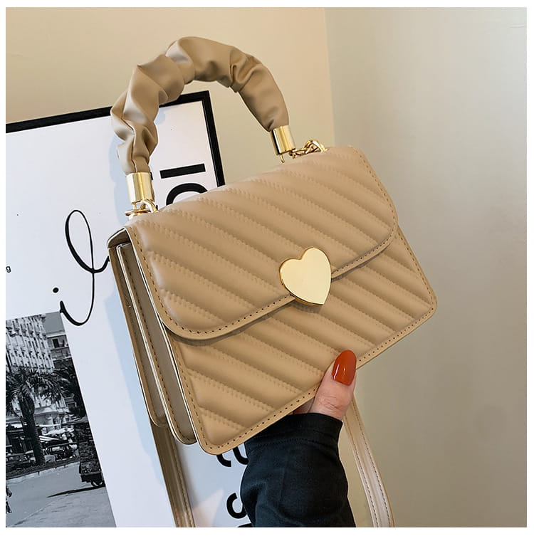 Beige quilted crossbody bag with ruched top handle and gold heart-shaped clasp.