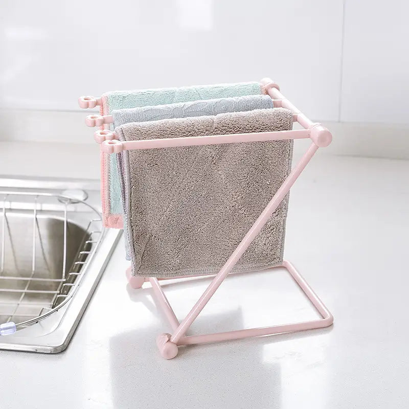 Pink plastic foldable dishcloth rack kitchen towel organizer shelf holding three textured towels in muted pastel shades