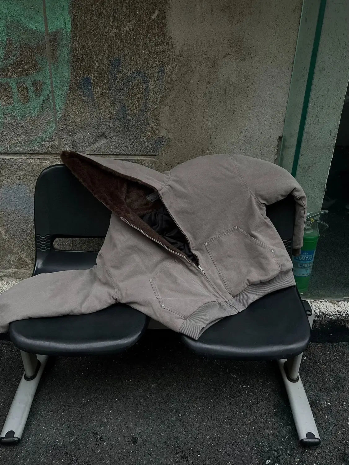 Abrigo acolchado de invierno de algodón con forro de piel sintética color beige, con forro interior en color marrón oscuro, colocado sobre un banco de plástico negro.