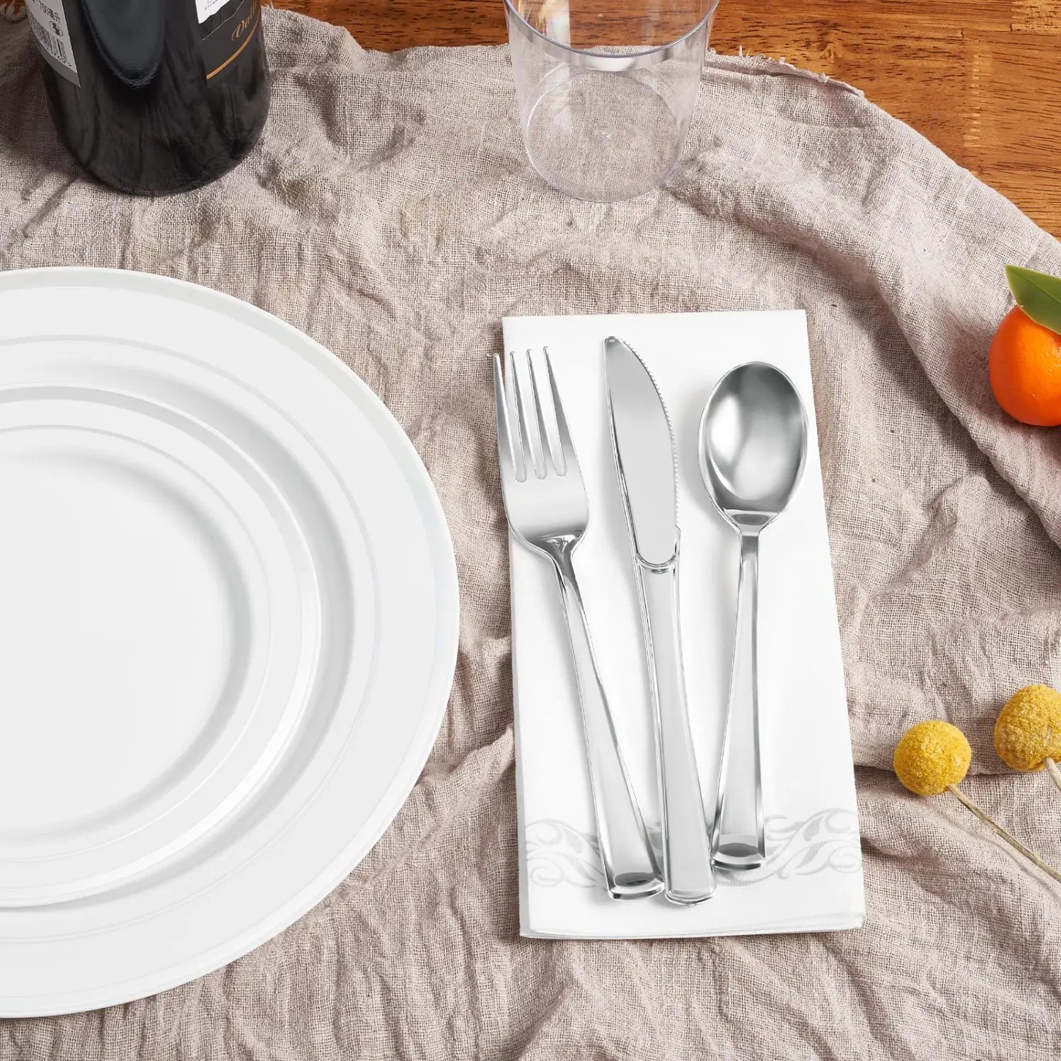 Set of three polished stainless steel cutlery pieces including fork knife and spoon neatly arranged on a white napkin for use with a plastic tableware set with gold rim plates for 50 guests.