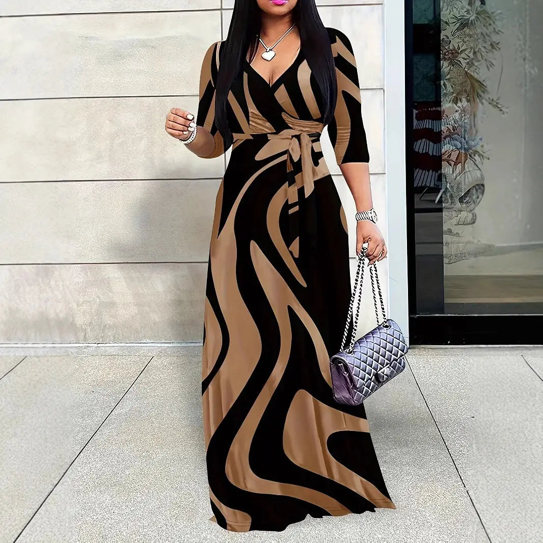 Une femme porte une élégante robe longue maxi à manches trois quarts imprimées, avec un imprimé audacieux de rayures ondulées noires et camel qui s’enroulent autour de la taille.