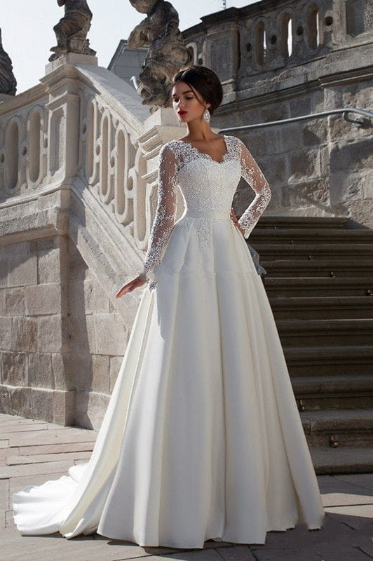 A woman wears an elegant long sleeve v neck lace back ivory wedding dress featuring lace sleeves and a flowing skirt.