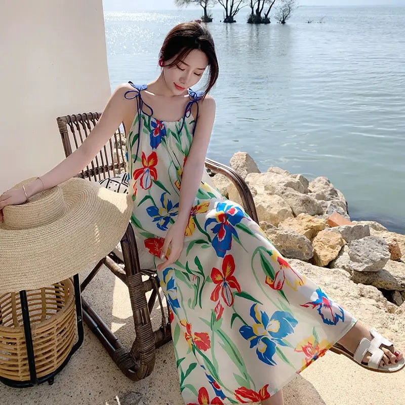 A woman wearing a floral mesh maxi dress with retro slip silhouette featuring vibrant red blue and green floral patterns on an off-white sleeveless summer dress.