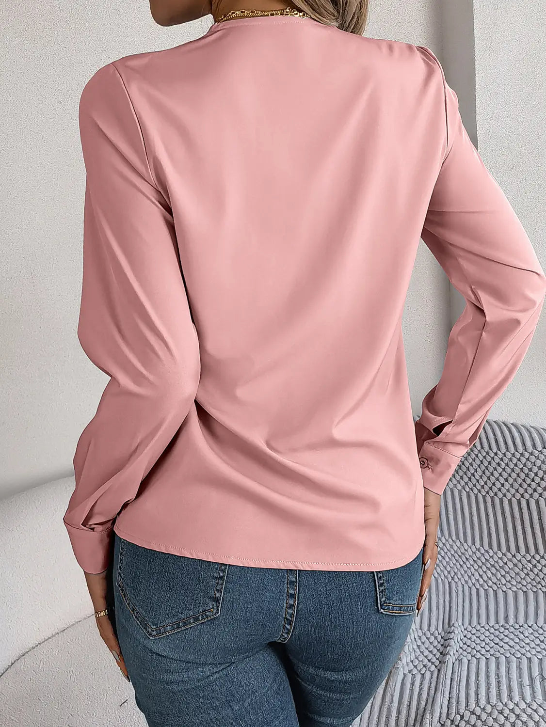 A soft pink satin blouse with long sleeves and subtle seam detailing resembling a white satin v neck wrap blouse with black trim.
