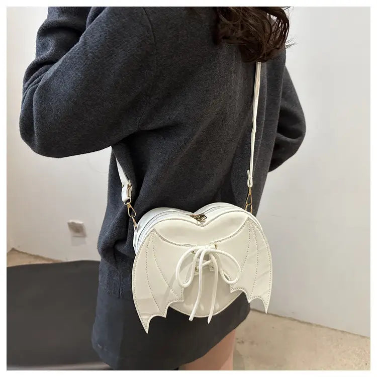 White bat-wing crossbody bag with glossy finish and lace-up front detail featuring a heart-shaped design.