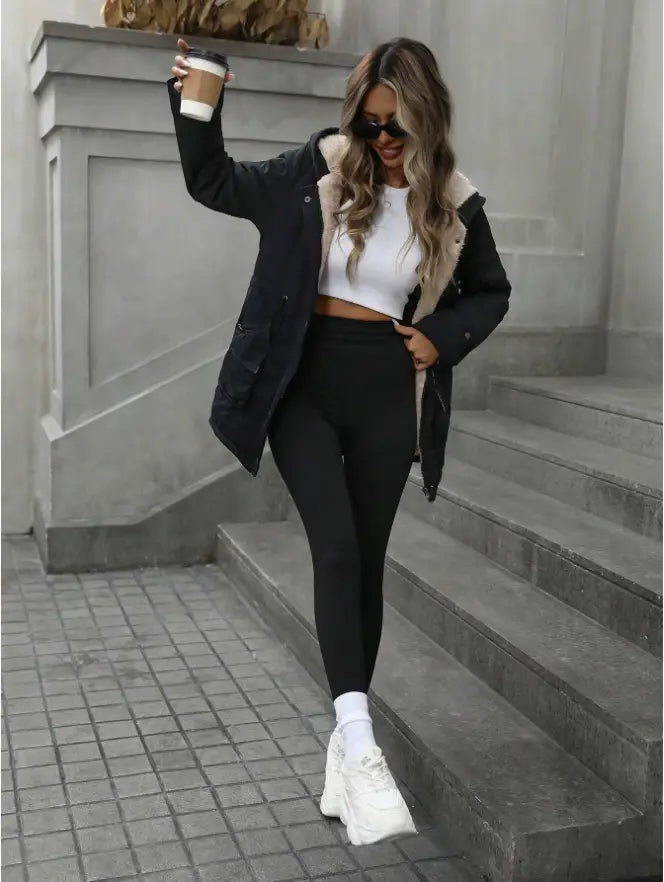 black shearling lined hooded zip up parka paired with a cropped white top and black leggings showcasing the coat’s exterior design