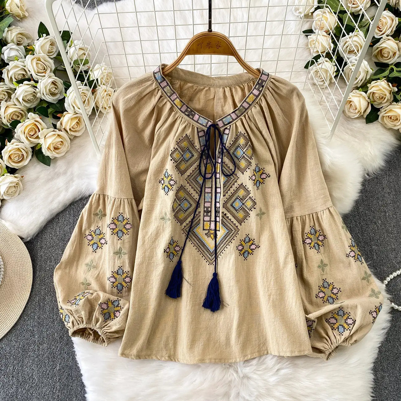 Beige embroidered lantern sleeve tie neck blouse with intricate yellow blue and pink geometric embroidery and a tie-front detail featuring navy tassels.