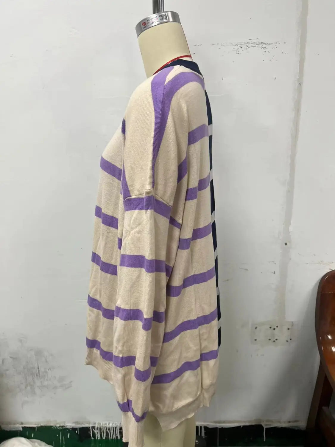 A cream-colored knit sweater with bold purple and black horizontal stripes displayed on a mannequin in a women’s oversized split color striped knit sweater design.