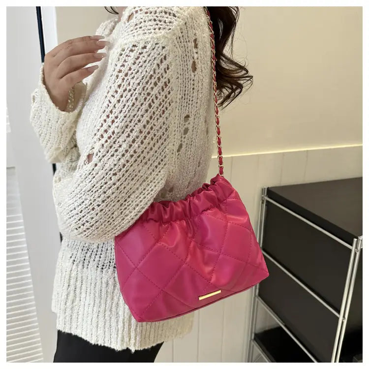 Fuchsia quilted satin crossbody bag with a chain strap made of faux leather for stylish shoulder wear.