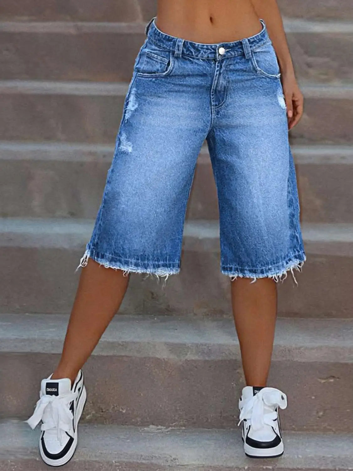 Pantalones capri de mezclilla azul desgastada con desgarros, con dobladillo deshilachado y bermudas de mezclilla de aspecto desgastado, y diseño clásico de cinco bolsillos.