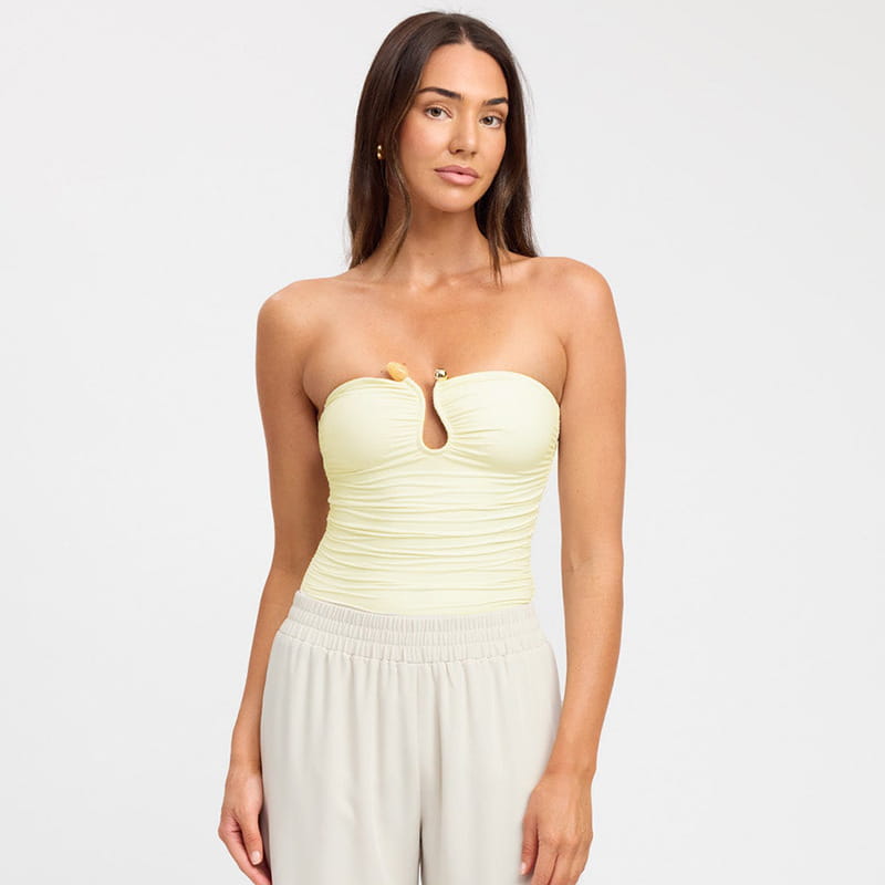 A pale yellow ruched strapless keyhole crop top featuring a central cutout with a small gold-toned clasp.
