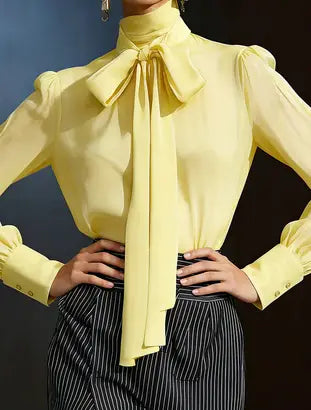 A pale yellow sheer chiffon puff sleeve satin bow blouse with a high collar and a large bow at the neckline.