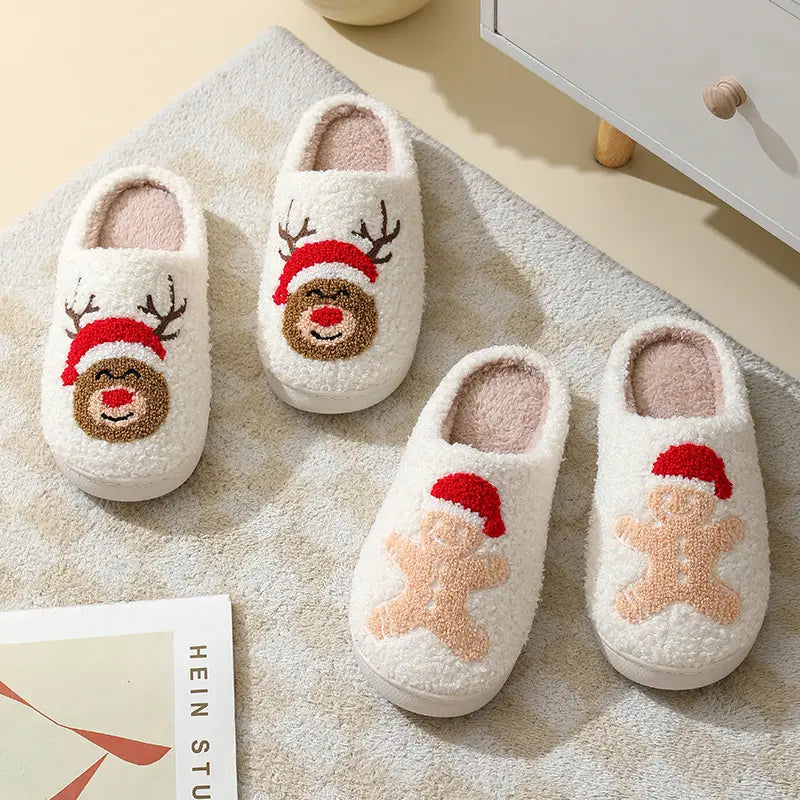 White fluffy slippers with cozy plush interiors featuring festive embroidered reindeer and gingerbread man designs wearing red hats for winter use.