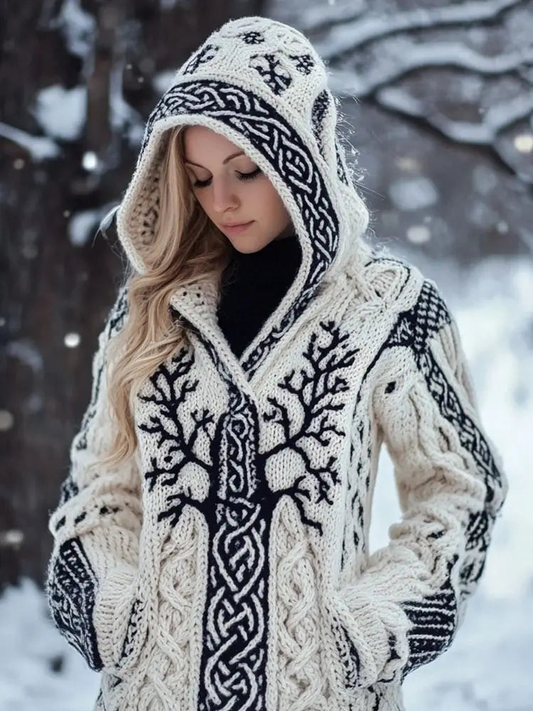 Cremefarbene, lockere Strickjacke mit langem Damenstil und weitem Rundhalsausschnitt, mit Kapuze, als Mantel mit kunstvollem schwarzem keltischem Knotenmuster und Lebensbaum-Motiven sowie kräftigen Zopfmuster-Details an Ärmeln und Vorderseite.
