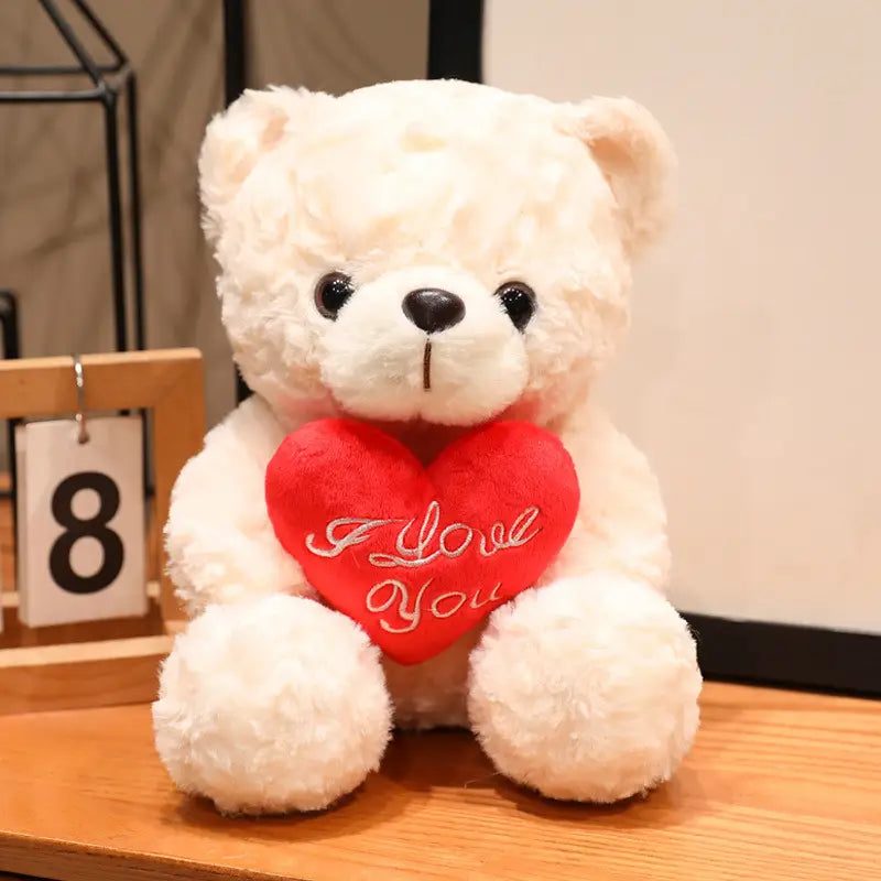 Ein weißer Plüsch-Teddybär hält ein rotes Herz, auf dem „I love you“ steht; als Valentinsgeschenk mit Rosen gezeigt, in Größen 16 bis 25 Zentimeter.