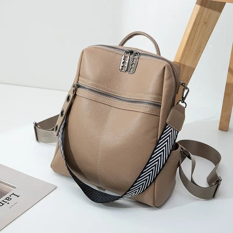 Beige urban faux leather backpack with silver-toned metal clasp and zipper featuring a contrasting black and white herringbone strap.
