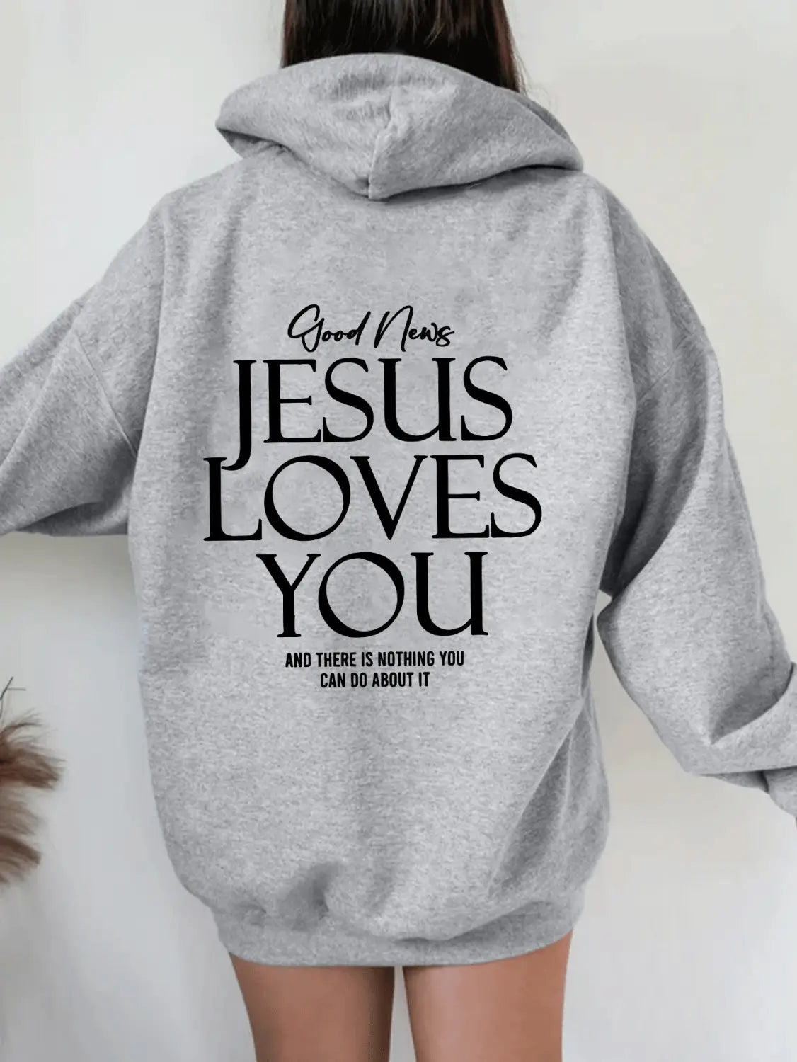 Gray hooded sweatshirt with black text reading good news jesus loves you and there is nothing you can do about it on the back side featuring an oversized streetwear style and kangaroo pocket.