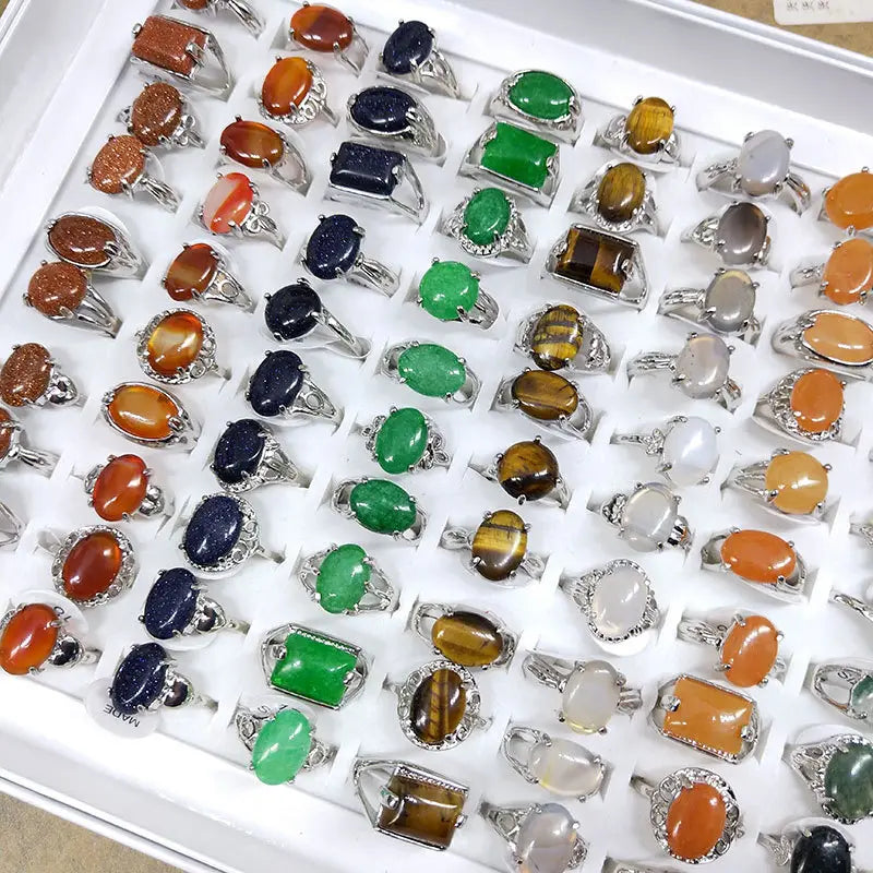 A collection of natural gemstone silver tone statement rings featuring oval rectangular and round cabochon gemstones in vibrant green orange blue brown and translucent white colors.
