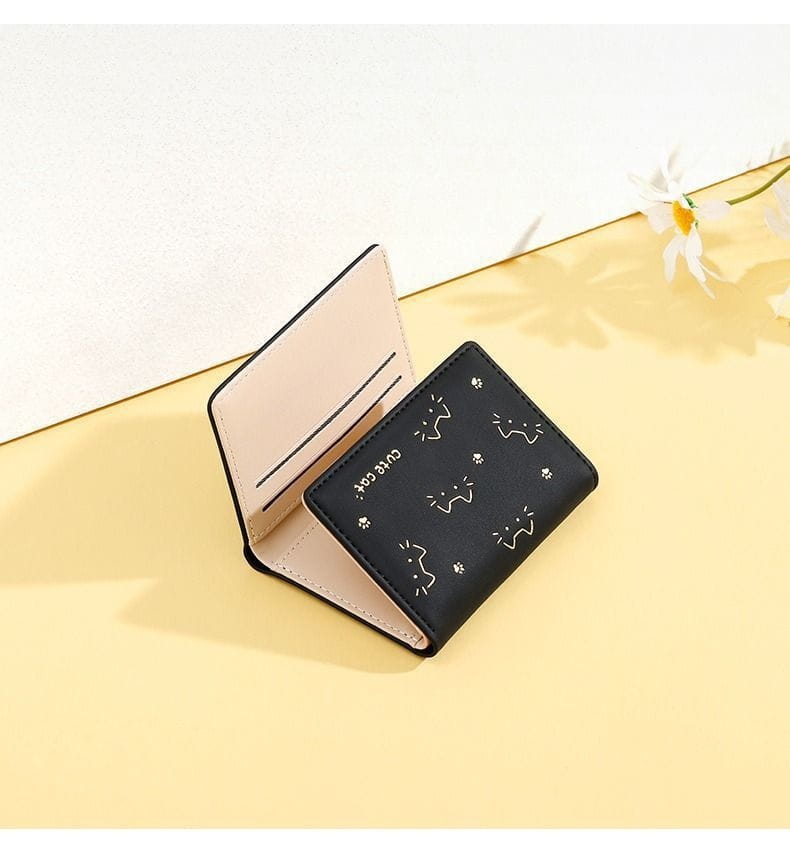 Black leather women’s small folding wallet with white cat face and paw print designs and beige interior.