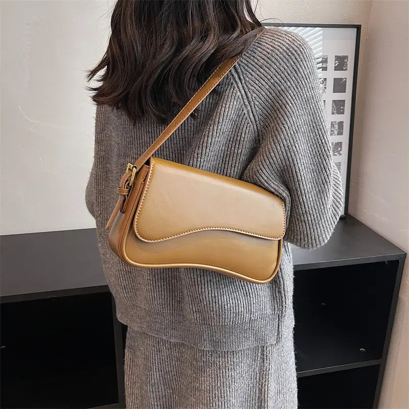 Tan leather messenger bag with a minimalist curved flap and gold-tone hardware designed as a crossbody organ bag.