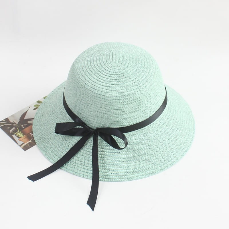 A mint green woven straw wide brim sun hat adorned with a black satin ribbon bow at the front.