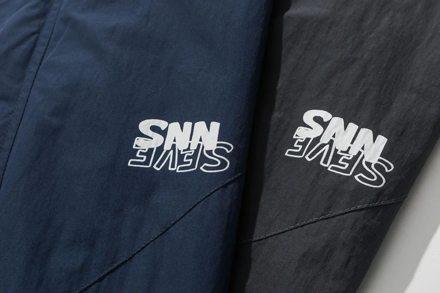 Pantalon de sport bleu marine et noir avec broderie du logo « snn » blanc, associé à une veste coupe-vent ample à blocs de couleurs brodés pour un usage décontracté et actif.