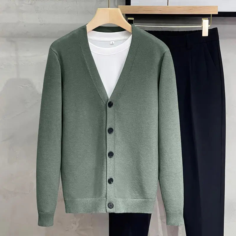 Ein weicher olivgrüner Herren-Strick-V-Neck-Cardigan-Sweater-Mantel mit schwarzen Knöpfen und gerippten Bündchen, der über einem weißen T-Shirt getragen wird.