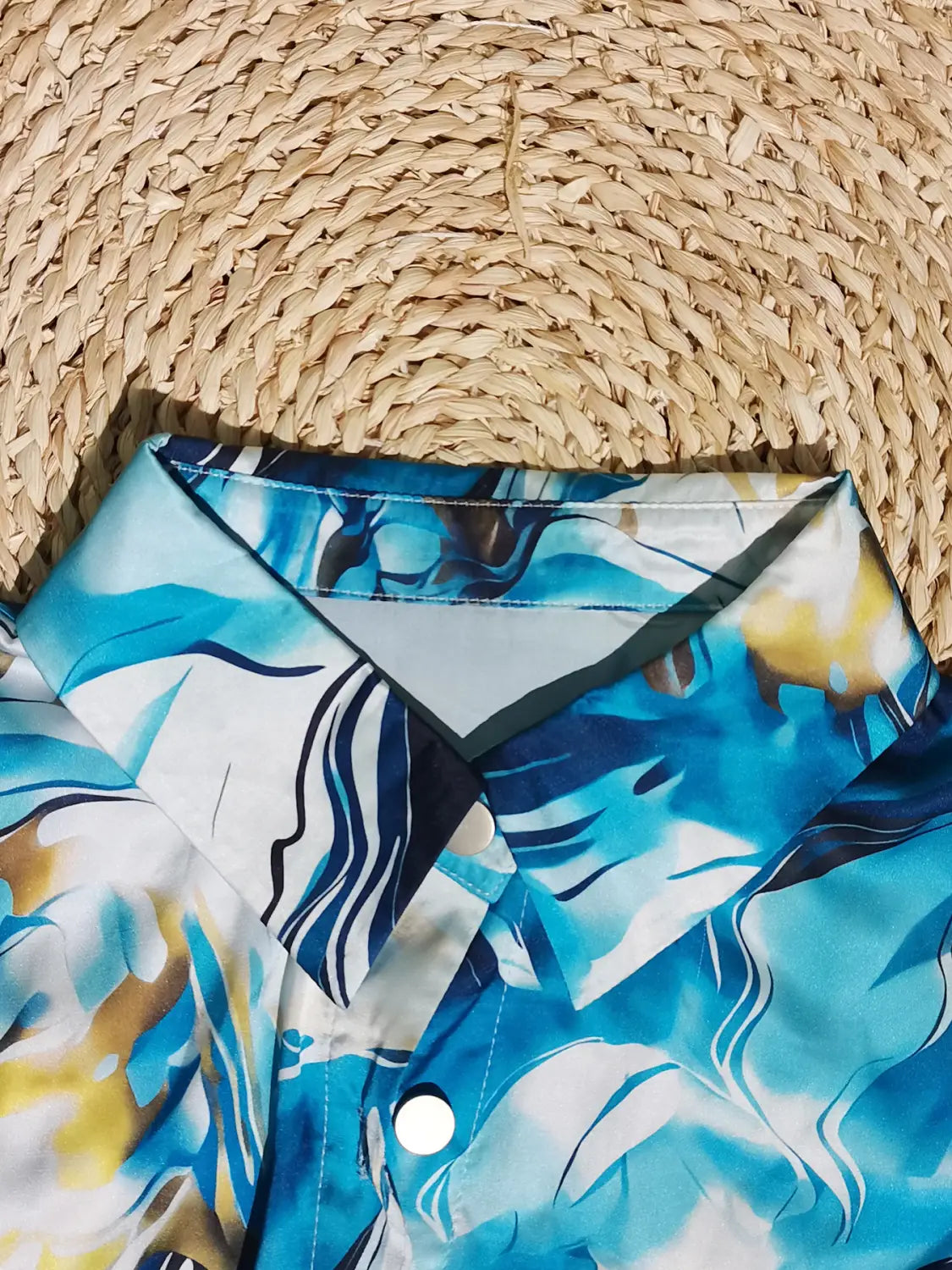 blue and white tropical print hawaiian shirt with a collar and buttons shown with a women’s marble print satin long sleeve button blouse.
