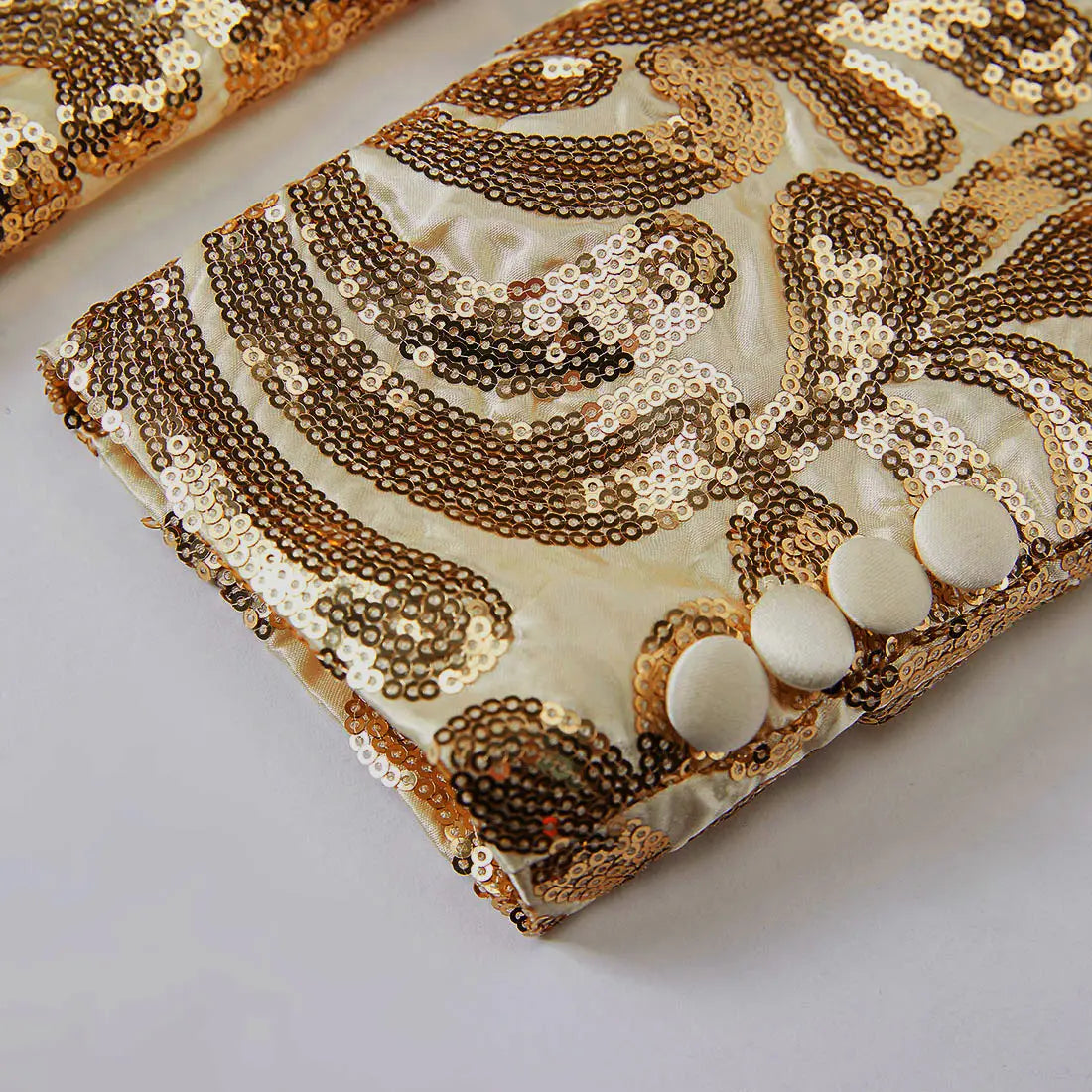 a luxurious cream-colored satin clutch with intricate gold and bronze sequin paisley patterns and three ivory buttons paired with a gold sequin mens suit jacket retro floral blazer