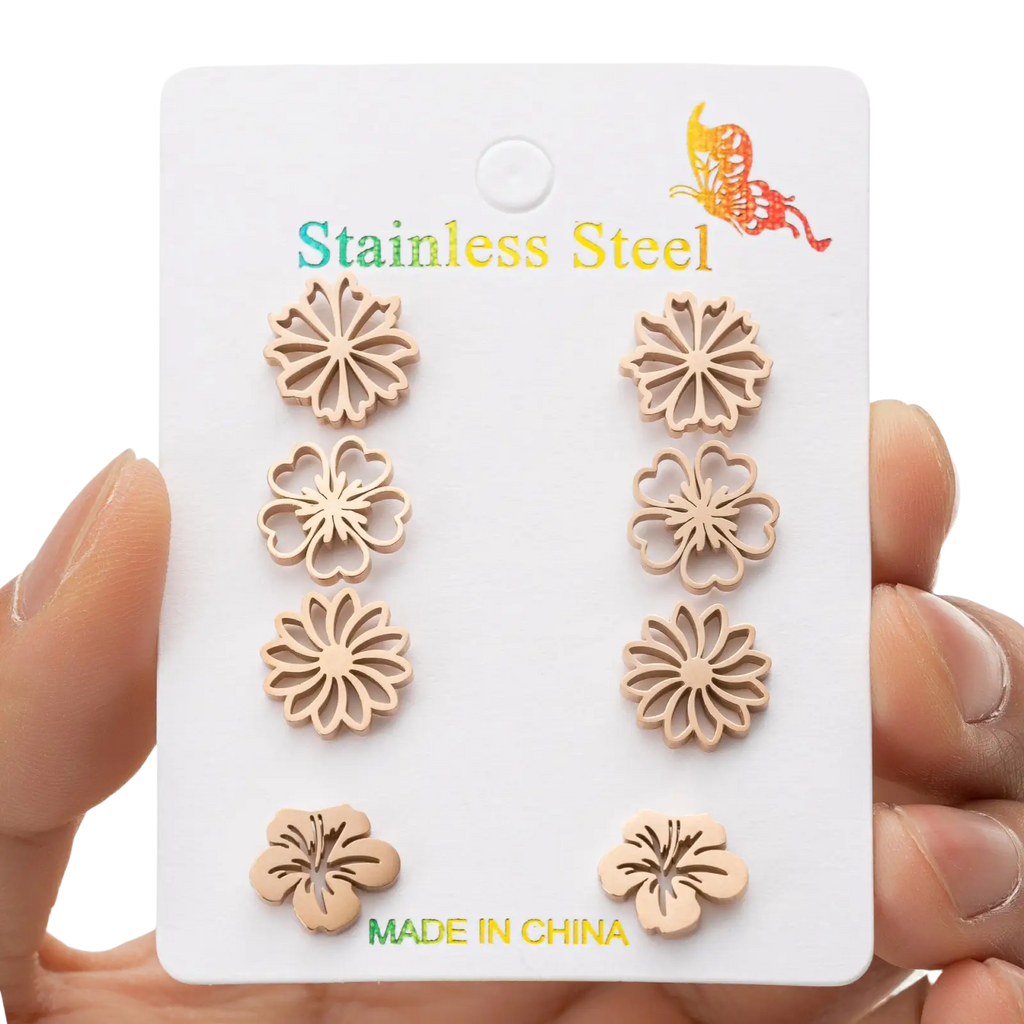 Set of six flower-shaped stainless steel stud earrings in light metallic finish displayed on a white card