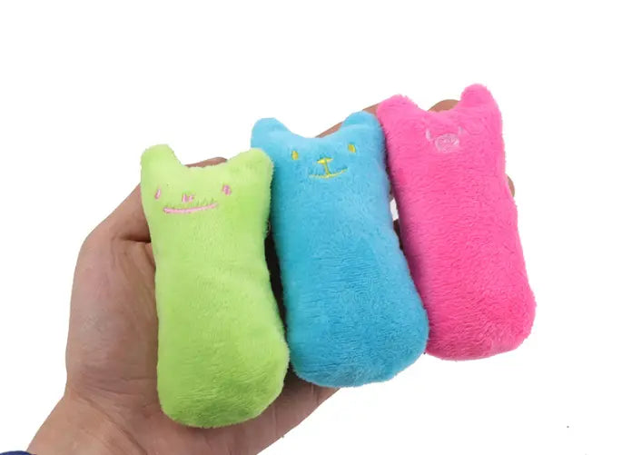Trois coussins pelucheux de jouets à base de cataire en forme de chat, aux couleurs vives, vert citron, bleu clair et rose éclatant, conçus pour le jeu interactif avec le chat.