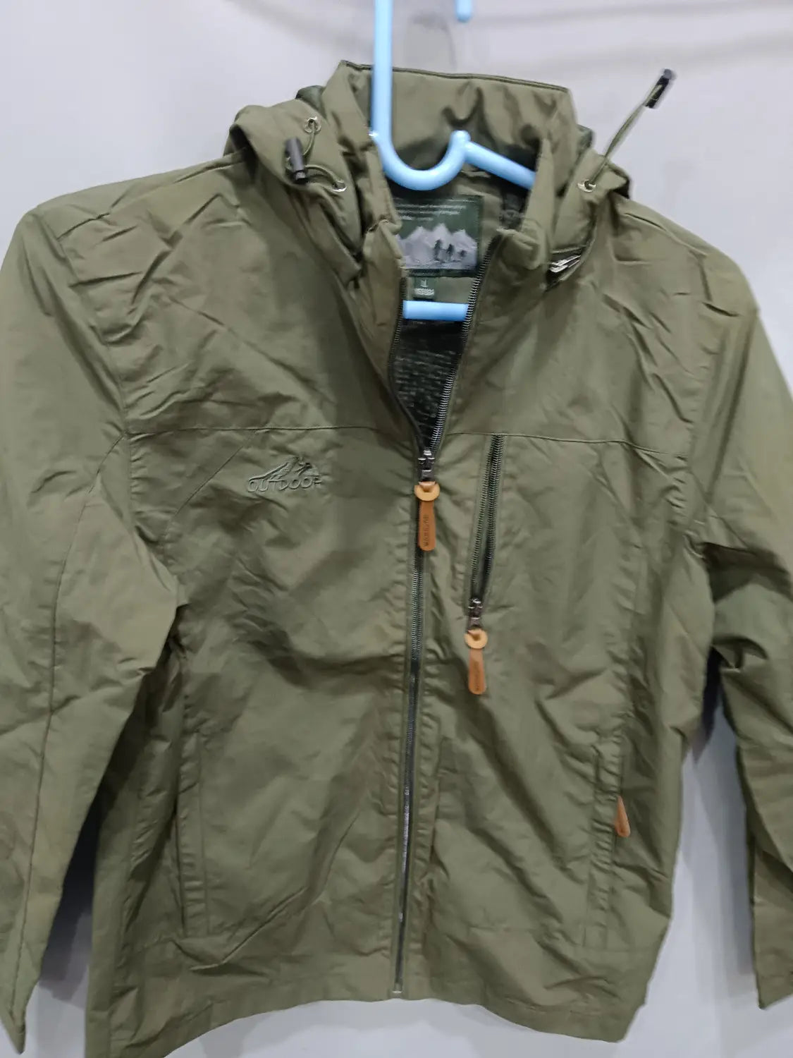 Chaqueta de senderismo con capucha impermeable color verde oliva, con cremallera frontal y bolsillos laterales, diseñada para actividades al aire libre.