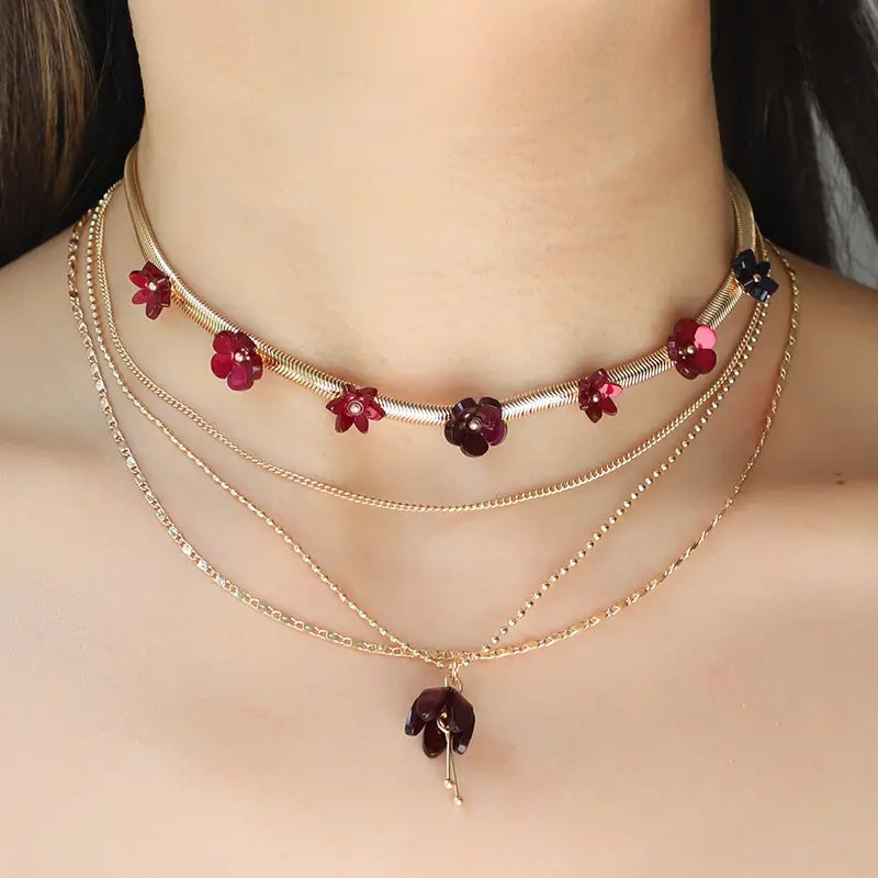A layered gold-toned choker necklace featuring red and purple acrylic floral charms and a delicate dangling pendant.