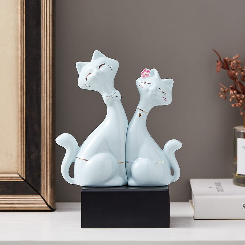 A delicate light blue ceramic figurine of two seated cats with a pink floral accessory and tiny bow tie for modern gold and white home decor.