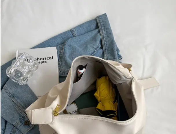 Leather shoulder bag with gold buckle and beige canvas tote featuring a gold-tone zipper and adjustable strap.