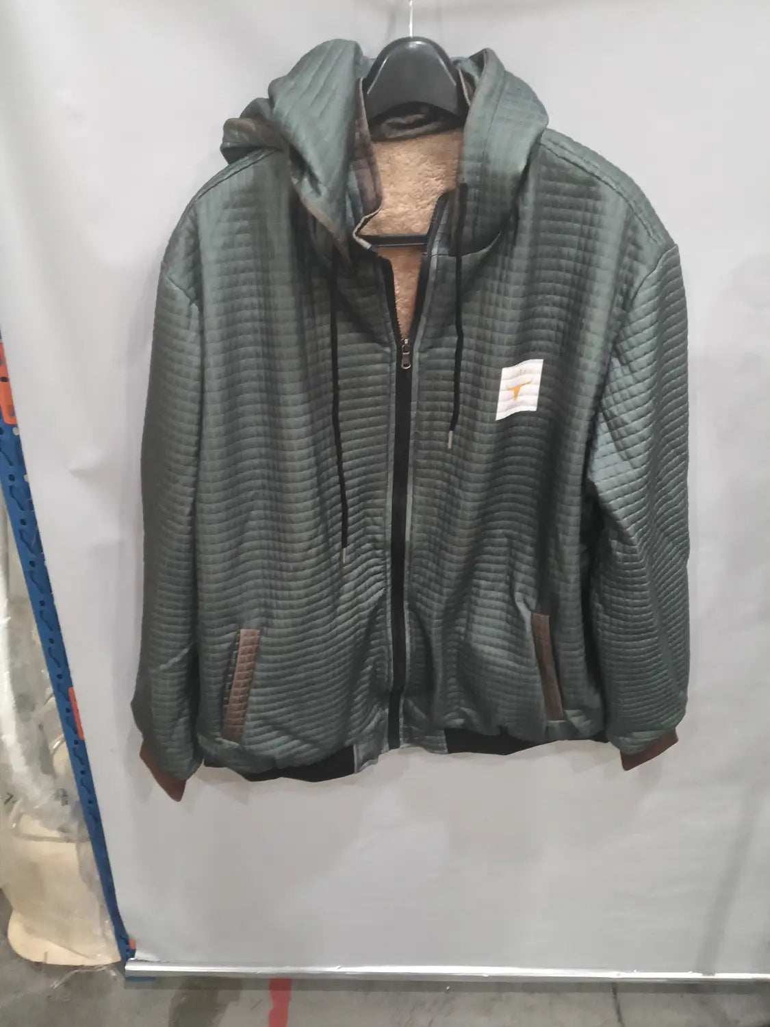 Veste à capuche zippée doublée de polaire pour homme en tissu matelassé vert foncé, fermeture éclair noire et passepoils marron sur les poches.