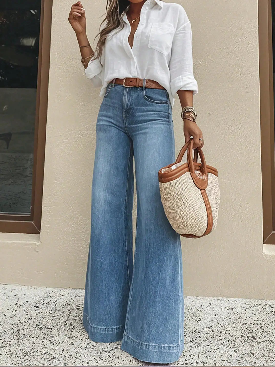 Eine geflochtene Strohtasche mit braunen Lederabschlüssen und Tragegriffen, kombiniert mit olivgrünen Denim-Jeans mit weitem Bein.