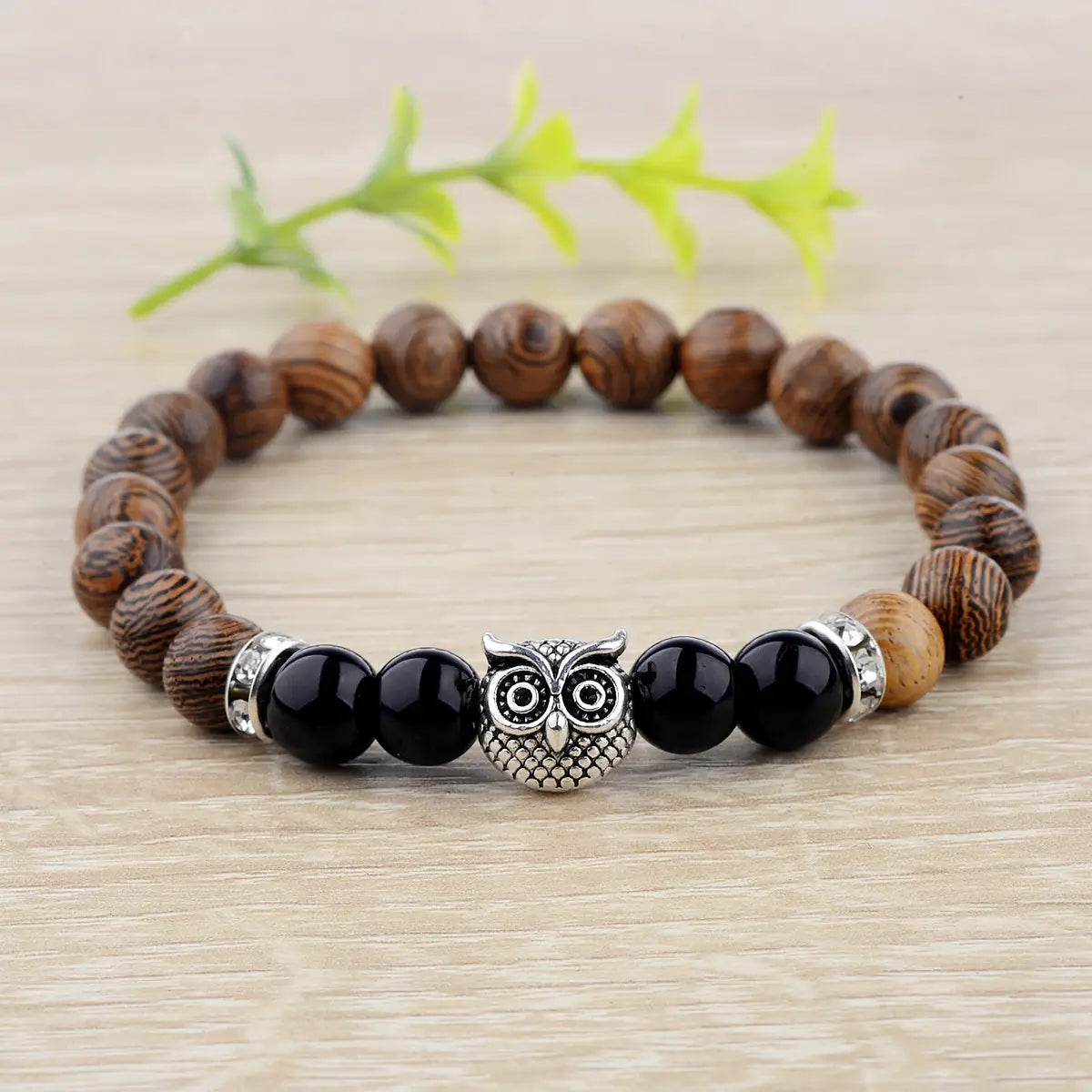 A silver owl charm wood and onyx beaded bracelet featuring dark brown wooden beads black onyx stones and metallic accents.